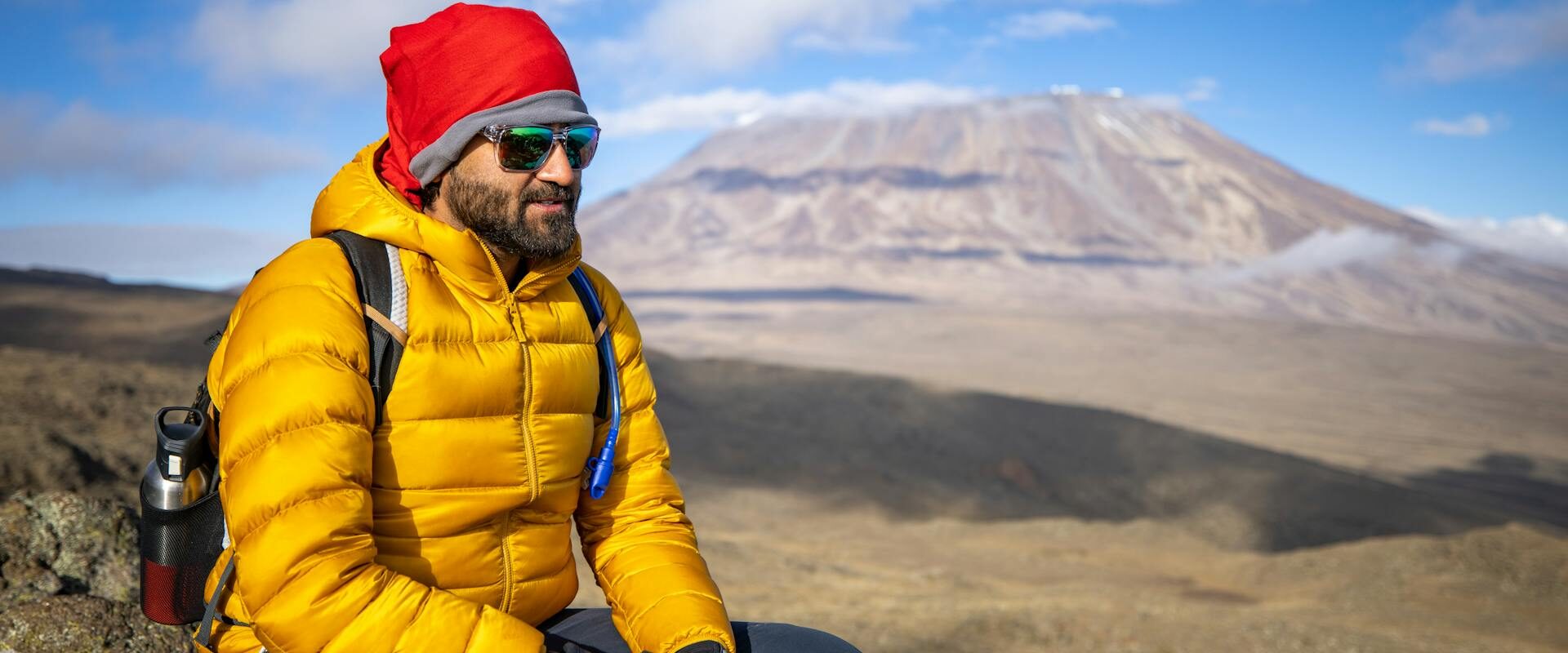 En man som sitter på en sten och vilar på väg upp för Kilimanjaro.