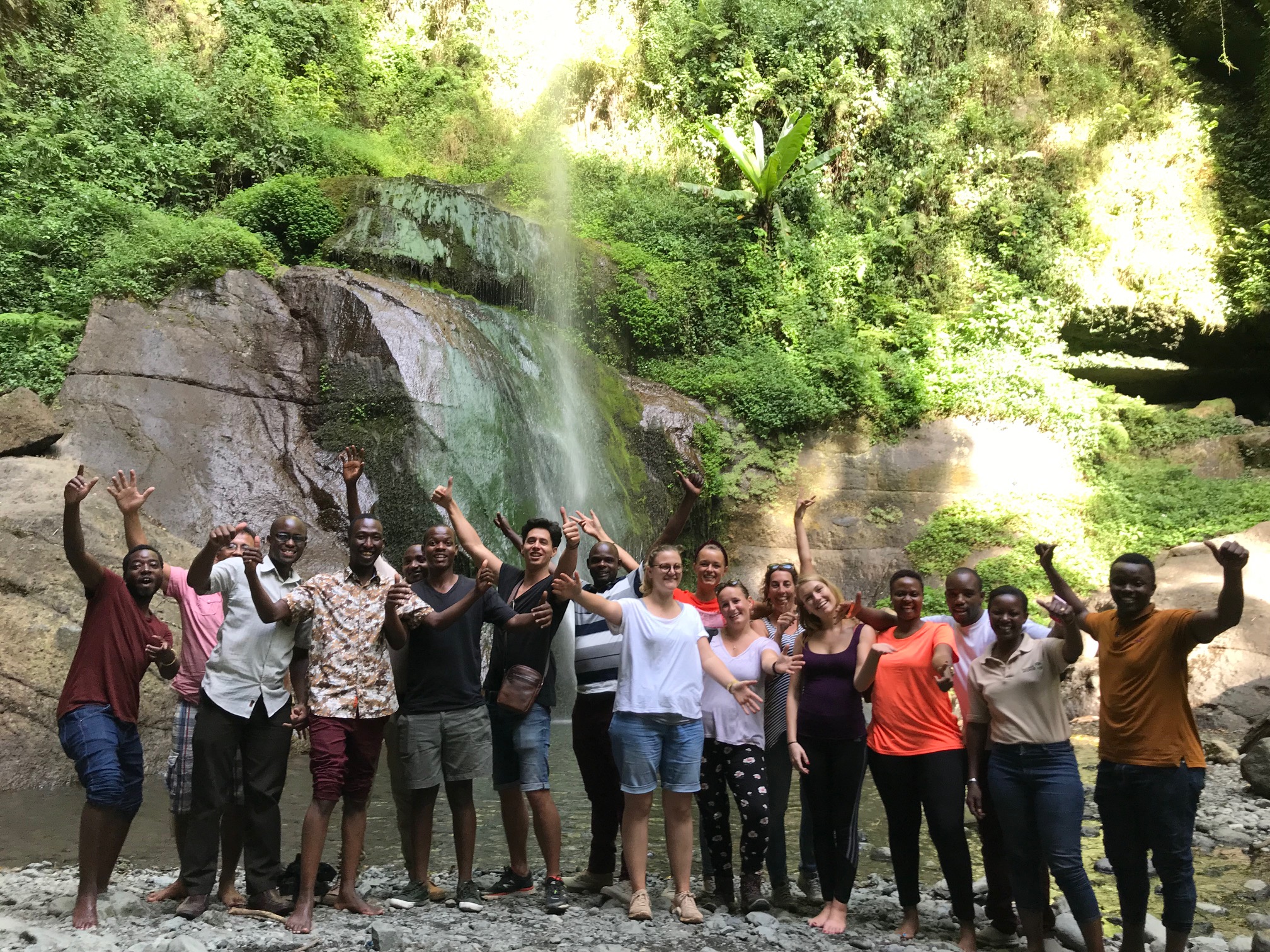 En grupp tanzanier och turister framför ett vattenfall i Tanzania.